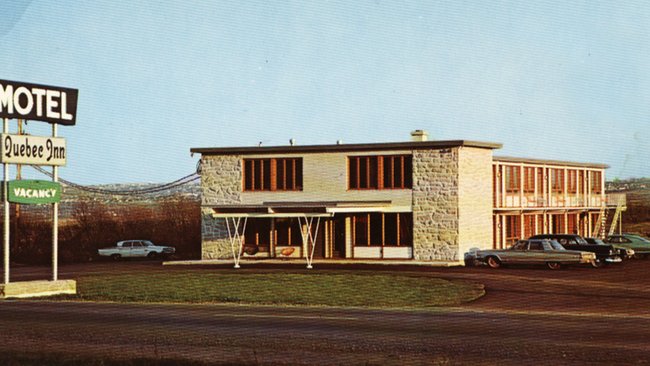 Une photo rétro du motel Québec Inn des années 70, montrant un bâtiment en pierre et bois entouré de voitures anciennes, symbolisant les débuts des Immeubles Jacques Robitaille inc.