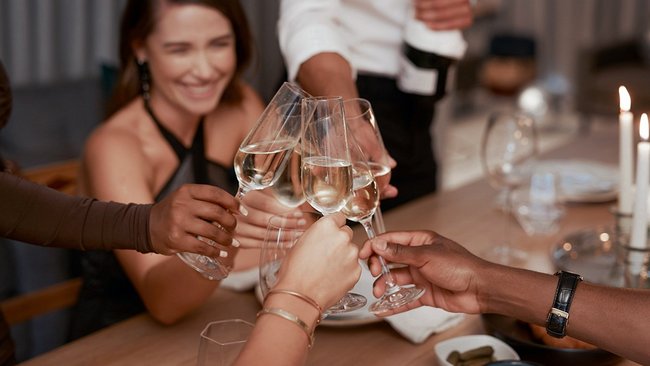 A group of people toast with glasses of white wine in a warm and elegant atmosphere. A smiling woman in the foreground reflects the festive and convivial atmosphere at L'Hôtel Québec.