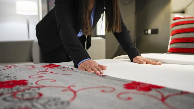 Une employée en train de préparer un lit avec soin dans une chambre décorée de tons rouges et blancs, illustrant les initiatives écologiques entreprises par les Hôtels JARO