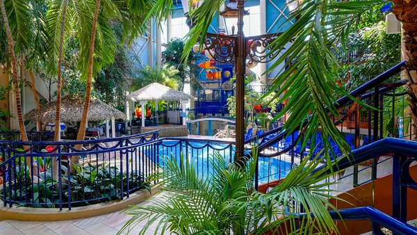 Indoor tropical pool at L'Hôtel Québec, featuring palm trees and water games. Perfect vacation atmosphere for the JARO Book Early and Save PROMO.