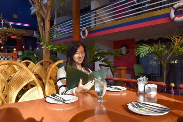 Smiling woman reading the menu at Les Palmes restaurant in Hôtel Québec Inn JARO, surrounded by a tropical ambiance with plants and warm decor.